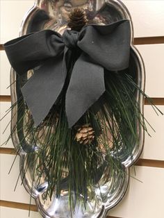 a pine cone and black bow on a silver platter hanging from the side of a wall