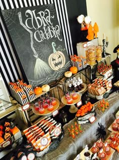 a table filled with lots of halloween treats and desserts on top of it in front of a chalkboard sign