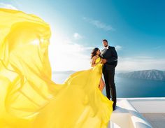 a man and woman standing on top of a building next to each other wearing yellow dresses