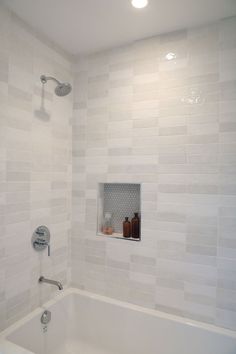 a white tiled bathroom with a tub and shower head