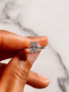 a woman's hand holding an engagement ring in front of her face and marble background