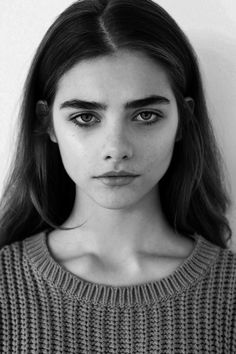 a black and white photo of a woman with long hair wearing a sweater looking at the camera