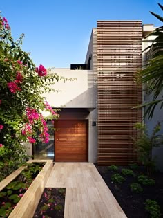 a modern house with wooden doors and flowers in the front yard, as seen from outside