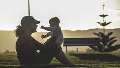 a woman sitting on the ground holding a baby in her lap and looking into the distance