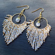 Discover the allure of our Moonstone Drops with Beaded Fringe, where classic elegance meets playful sophistication. These earrings showcase stunning moonstones, renowned for their mystical adularescence--a captivating glow that shifts as you move. Each moonstone is set in a luxurious 24K gold electroplated setting, which enhances the stone's natural luminescence. The design is further elevated by a fringe of delicately beaded accents that dangle gracefully from the base of each 24k gold plated circle. The beaded fringe adds a dynamic element to the earrings, creating a gentle swaying effect that catches the light beautifully. The combination of the moonstone's ethereal glow with the intricate beaded detail makes these earrings a perfect statement piece for any occasion. These earrings are Bohemian White Moon Shaped Jewelry, Bohemian White Moon-shaped Jewelry, Handmade White Crystal Round Earrings, Handmade White Crystal Earrings, White Wire Wrapped Bohemian Earrings, Handmade White Teardrop Crystal Earrings, White Bohemian Wire Wrapped Earrings, Bohemian White Wire Wrapped Earrings, White Handmade Moon-shaped Earrings