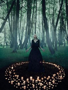 a woman standing in the middle of a forest surrounded by candles