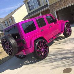 a pink jeep parked in front of a house with purple wheels and rims on it