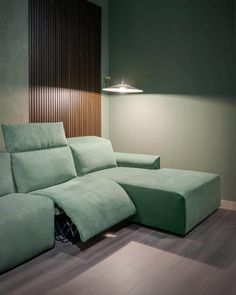 a green couch sitting on top of a hard wood floor next to a wall mounted lamp