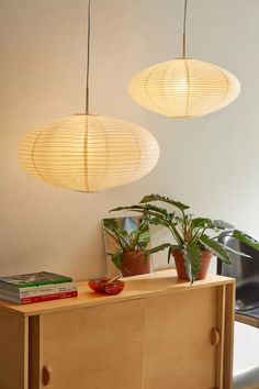 two lamps hanging from the ceiling above a wooden cabinet with books on it and a potted plant