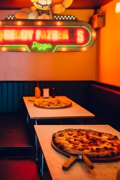 two pizzas sitting on top of tables in front of a neon sign that reads yellow papa's