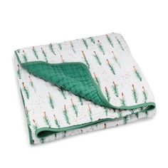 a green and white blanket laying on top of a white sheet with trees printed on it