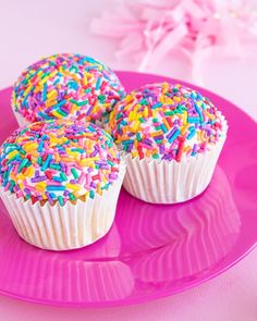 three cupcakes with sprinkles on a pink plate