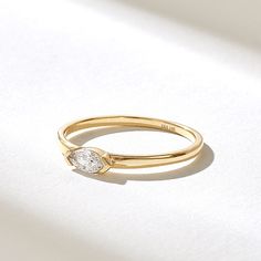 a yellow gold ring with a single diamond on the top, sitting on a white surface