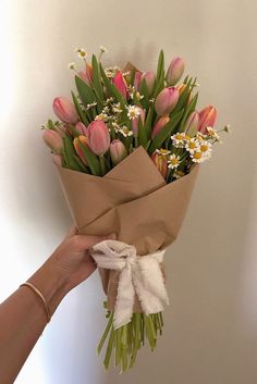 a person holding a bouquet of tulips and daisies in brown paper wrap