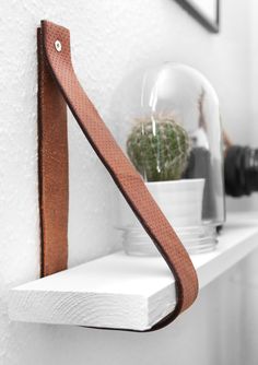 a white shelf with a brown leather strap hanging from it's side and a potted plant in the corner