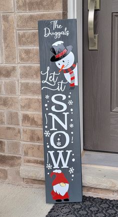 a wooden sign that says let it snow on the front porch with santa hats and mittens