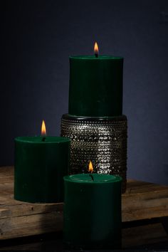 three green candles sitting next to each other on top of a wooden table in front of a dark background