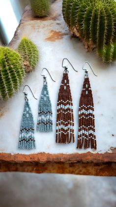 three pairs of beaded earrings sitting on top of a table next to a cactus