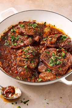 a large pot filled with meat and vegetables on top of a white counter next to a spoon