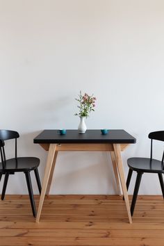 two chairs and a table with a vase on it in front of a white wall