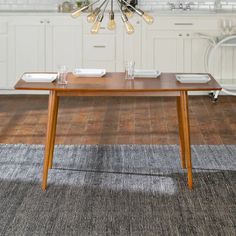 a wooden table with plates and glasses on it in the middle of a large kitchen