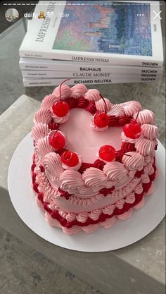 a heart shaped cake with cherries on top sitting on a table next to a stack of books