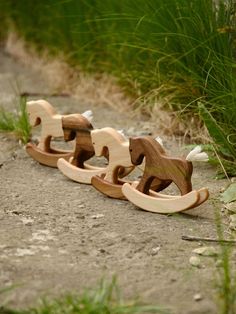 three wooden rocking horses sitting on the ground in front of some tall grass and weeds