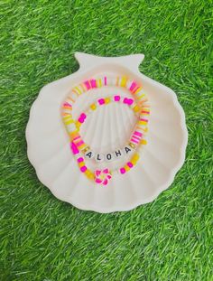 a personalized scallop shell on the grass with beads around it that says aloha