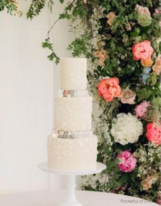 a three tiered white wedding cake sitting on top of a table next to flowers