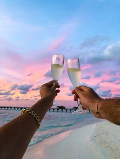 two people toasting with wine glasses on the beach at sunset in front of an ocean