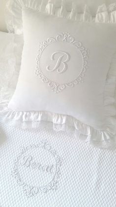 a white bed with ruffled pillows and a monogrammed pillow