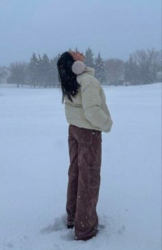 a woman standing in the snow with her back turned to the camera, wearing brown pants and a white jacket