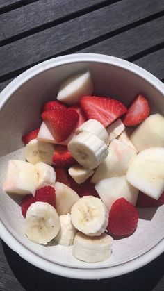 a white bowl filled with sliced up bananas and strawberries on top of a wooden table