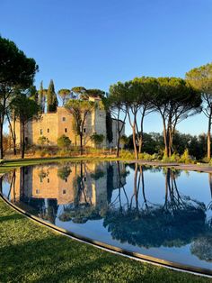 a large pool surrounded by trees in front of an old building with its reflection on the water