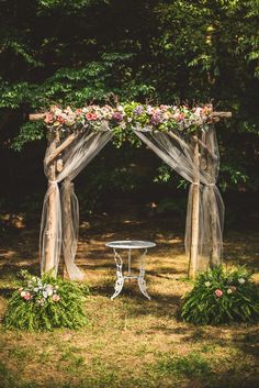 an outdoor wedding setup with flowers and sheer fabric on the arbor, surrounded by lush greenery