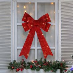 a red bow hanging on the side of a window in front of a christmas wreath