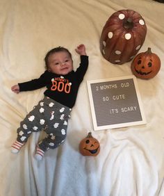 a baby laying on top of a bed next to two pumpkins and a sign