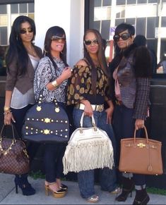 four women standing next to each other holding purses