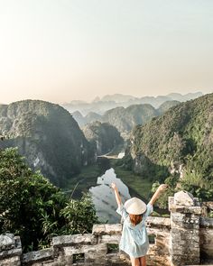 a woman standing on top of a stone wall with her arms up in the air