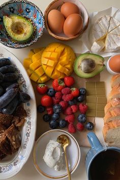 an assortment of food on a table including bread, fruit, eggs and yogurt