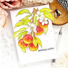 a birthday card with peaches and flowers on it next to a pen, flower pot and paperweights