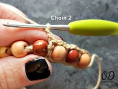 a person holding a crochet hook with beads on it's end, and another hand holding a pair of scissors