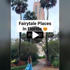 a woman in a blue dress walking down a path with palm trees and a clock tower behind her