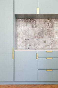 a kitchen with blue cabinets and gold pulls on the handles, marble counter tops, and wooden flooring