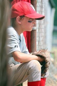 a young boy wearing a red baseball cap sitting on a bench