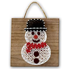 a string art snowman is hanging on a wooden plaque, with red and white beads