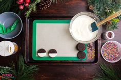 a tray with cookies, cream and sprinkles on it next to christmas decorations