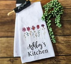 two personalized kitchen towels with flowers on them next to a sprig of green leaves