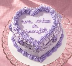 a heart shaped cake with purple frosting sitting on a glass plate next to a pink tablecloth