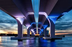 the underside of a bridge over water at dusk with lights reflecting off it's sides